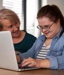 Down syndrome woman using computer with help of her mother