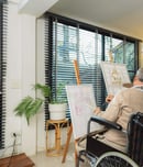 Elderly men ride a wheelchair doing hobby activity by painting in art school. Happy retired people having fun using creativity and practicing drawing at home.
