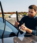 Man is changing windscreen wipers on a car while standing at the street. Male replace windshield wipers on car.