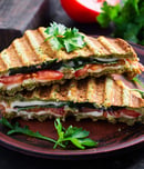 Vegetarian sandwich panini with spinach leaves, tomatoes and cheese on a dark table. Toast with cheese.