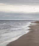 View of a man walking along the coastline enjoying the beach waves under the cloudy sky