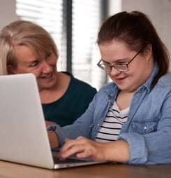 Down syndrome woman using computer with help of her mother