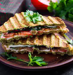 Vegetarian sandwich panini with spinach leaves, tomatoes and cheese on a dark table. Toast with cheese.