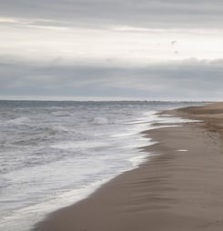 View of a man walking along the coastline enjoying the beach waves under the cloudy sky