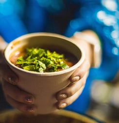 woman seller holds a soup in a disposable eco-dish in her hands.