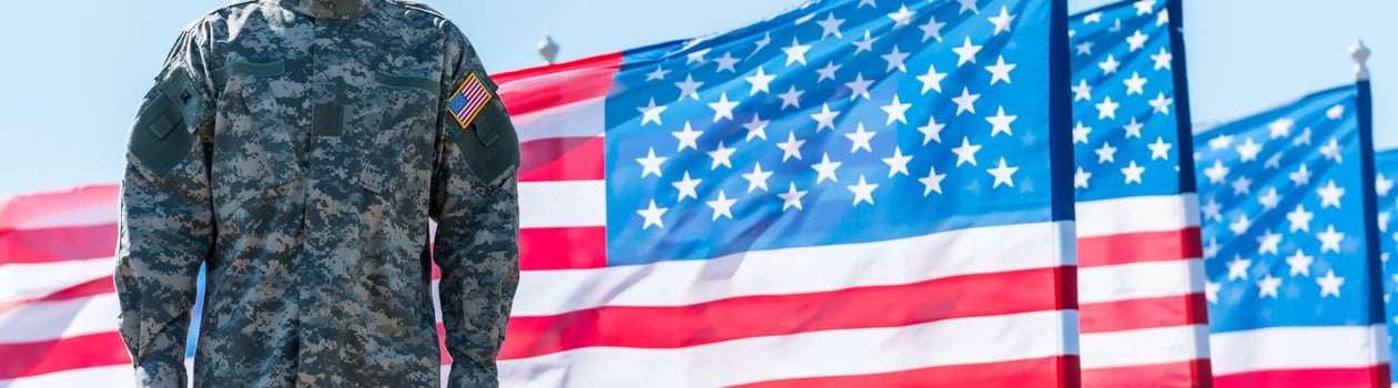 soldier in uniform standing near american flags against blue sky