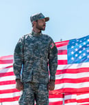 soldier in uniform standing near american flags against blue sky