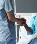 Elderly African American patient smiling to nurse while she holding his hands during her visit in ward