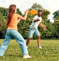 Happy young father with his daughter playing frisbee in the meadow in the park, having fun together on a warm sunny day off.