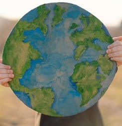 Protection and love of earth. Little boy holding planet in hands against green spring background. Earth day concept. Environmental Conservation