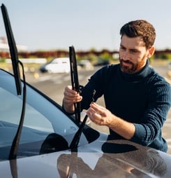 Man is changing windscreen wipers on a car while standing at the street. Male replace windshield wipers on car.