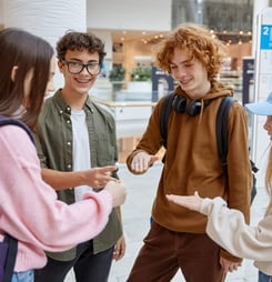 Teenagers friends playing rock-paper-scissors hand game while standing in hall of big shopping mall