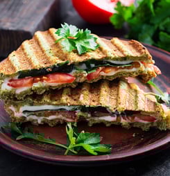 Vegetarian sandwich panini with spinach leaves, tomatoes and cheese on a dark table. Toast with cheese.
